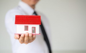 Businessman Holding Model House In Palm Of Hand
